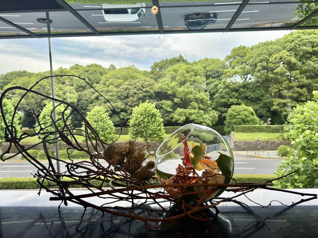 金魚鉢のような器にいけられた、キウイツルとモンステラの涼しげな作品(花材:アンスリウム、すぐり、バードネストなど)